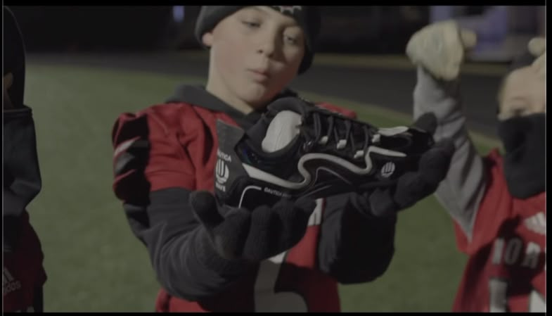 A young athlete holding a pair of cleats donated through the foundation.